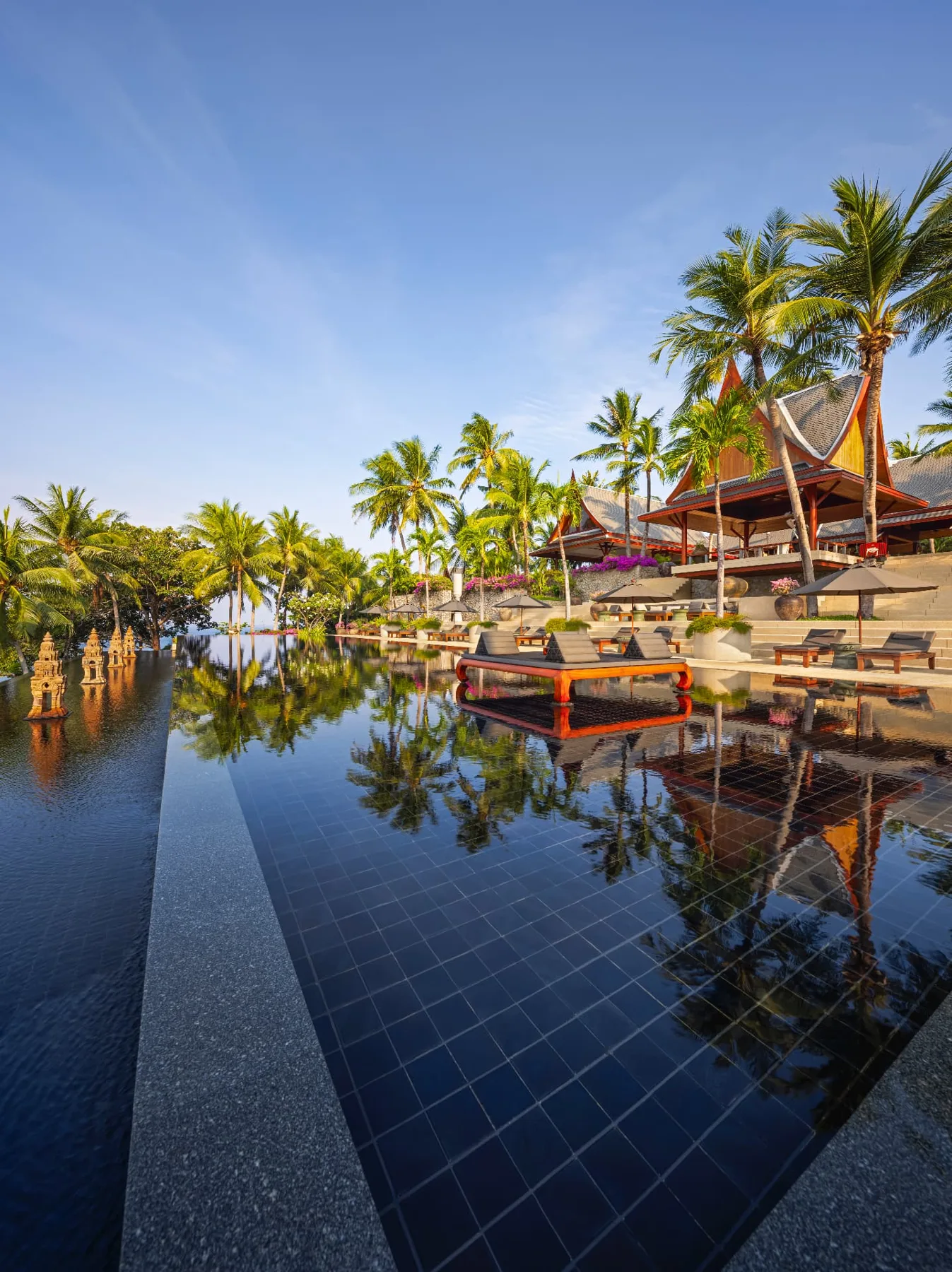 Reflections of palms and pavilions in the black-tiled infinity pool