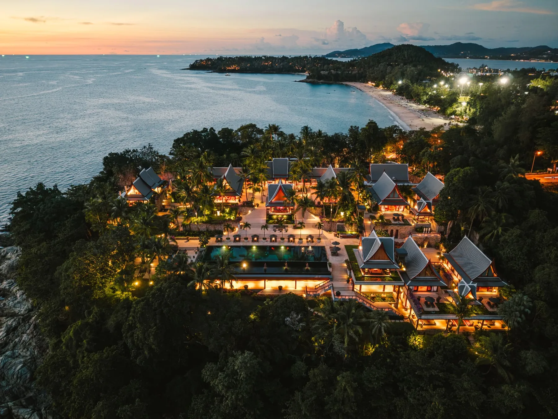 The estate's Thai pavilions illuminated at dusk above Surin Beach